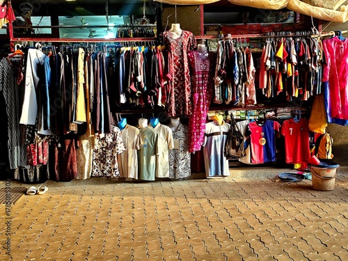 Street-side market stall with vibrant, assorted clothes hanging on racks and displayed on mannequins over a textured pavement