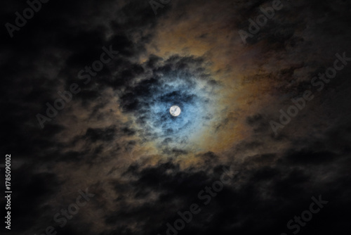 Moon shines through clouds with dramatic blue and gold colored halo 