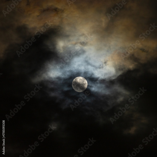 Moon shines through clouds with dramatic blue and gold colored halo 