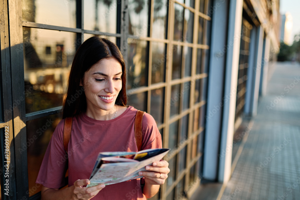 Fototapeta premium Portrait of a smiling young woman looking at a map in the city, tourists visiting destination, summer trip exploring