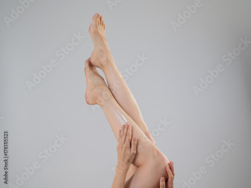 Woman applying moisturizer to her legs. White background. 