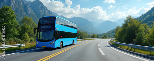 Blue double decker bus travels on a winding mountain road. Rich green trees line the asphalt highway under a bright sunny sky with white clouds. Scenic landscape view.