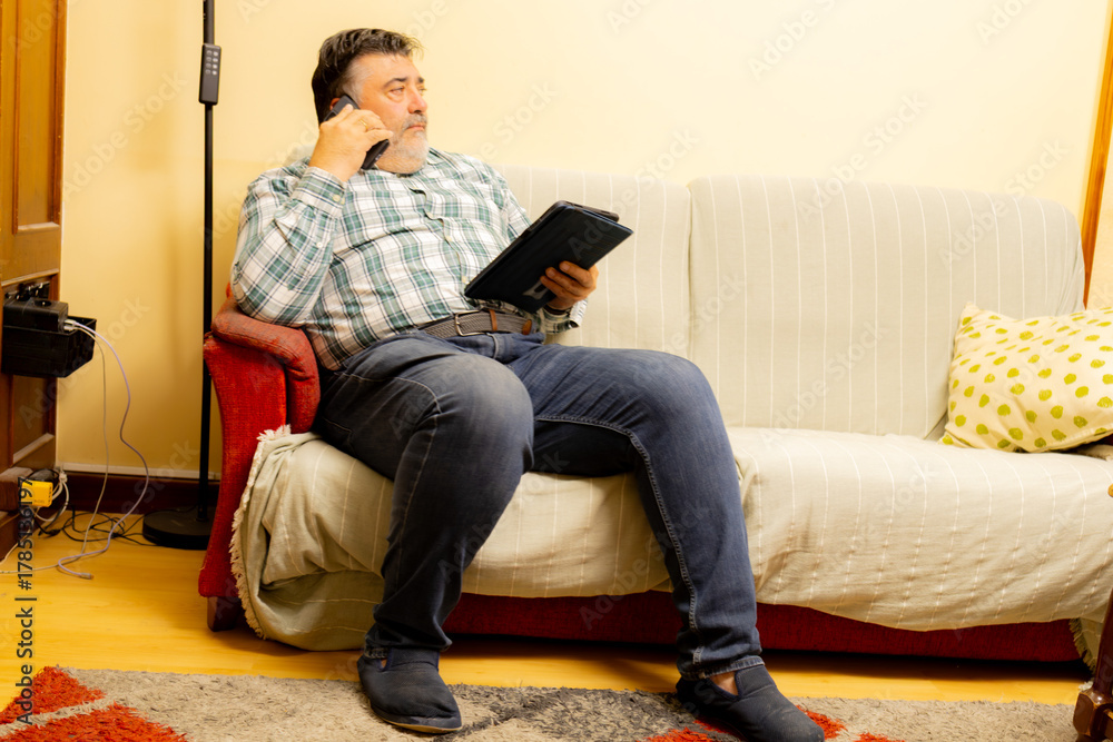 Fototapeta premium Man multitasking on phone call and tablet on couch