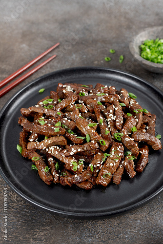 Fried teriyaki beef with sesame seeds and green onions on a brown background. Asian cuisine.