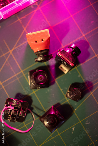 various fpv drone cameras and components displayed on a green cutting mat with vibrant lighting, neutral background, clear negative space, clean composition, balanced framing, minimalist layout