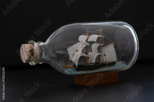 Ship in a Bottle. Small ship model in a bottle with a cork stopper on black background.