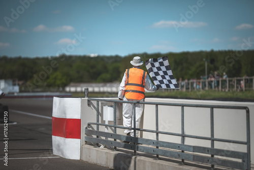 Tableau sur toile Race official waving checkered flag at the finish line of a motorsport event