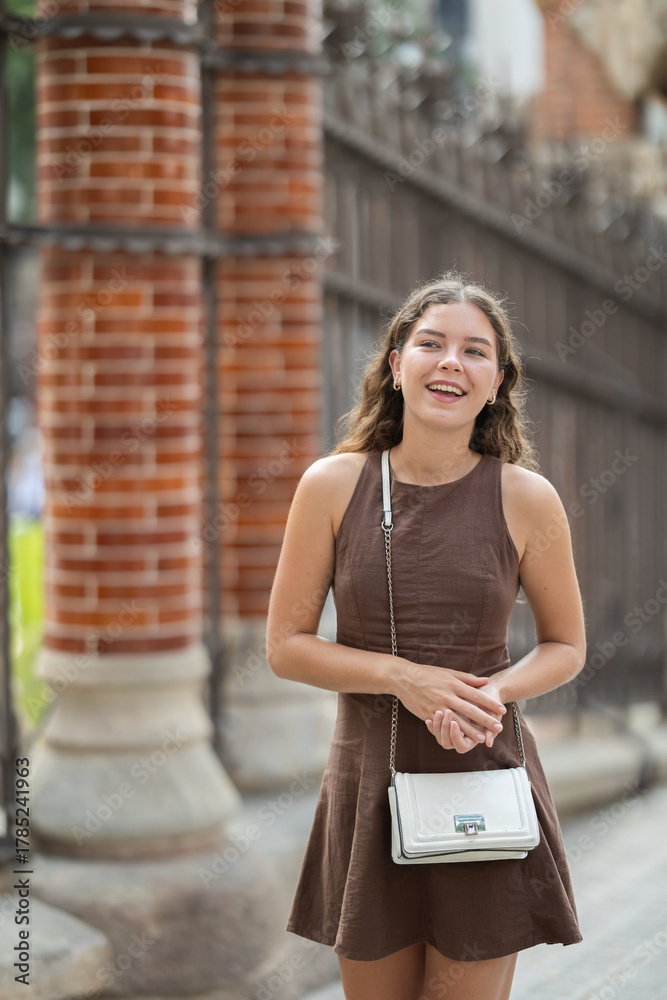 Fototapeta premium Young female tourist dressing in short dress enjoying walk near columns of architectural complex of Hospital