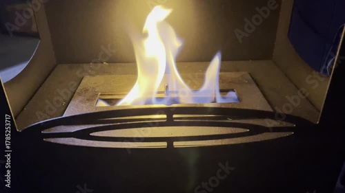 This video shows a close-up of a modern, portable bioethanol fireplace burning in a dark setting. Bright, dancing flames emerge from a rectangular burner.