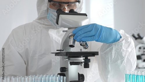 Foto Medical virologist in protective hazmat gear examining viral samples under a mic
