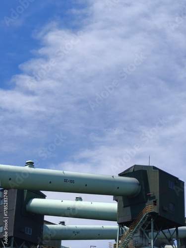Industrial pipes and machinery structures against cloudy blue sky