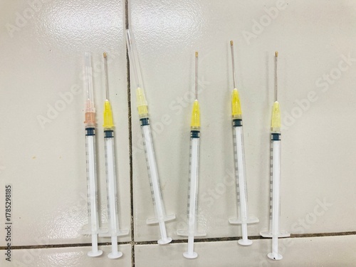Multiple disposable syringes with yellow caps on tiled surface