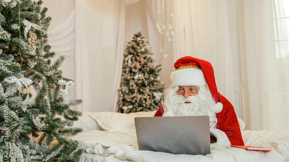 Fototapeta premium santa claus using a laptop computer in a festive christmas setting