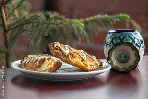 Frontal photograph of empanadas with sauce seen from the front on a white plate on a Corinthian table