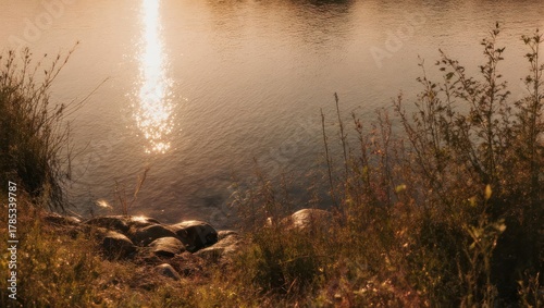 Calm lake reflecting the warm light of a setting sun, with grassy foreground and rocky shore