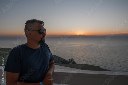 A man in sunglasses swims in a blue pool. Vacation at the hotel by the sea, sunset and mountains. Happy dad, family happiness. Muscles and a beautiful figure, black hair. High quality photo