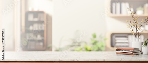 Fototapeta Naklejka Na Ścianę i Meble -  Books and ceramic vase aside potted plant on marble table across bookshelf in a bright living room.