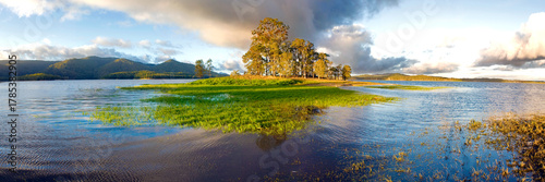 Golden afternoon light over a flooded lakeshore and grassy island surrounded by hills.