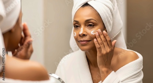 Photograph of a woman in a bath robe applying facial cream 