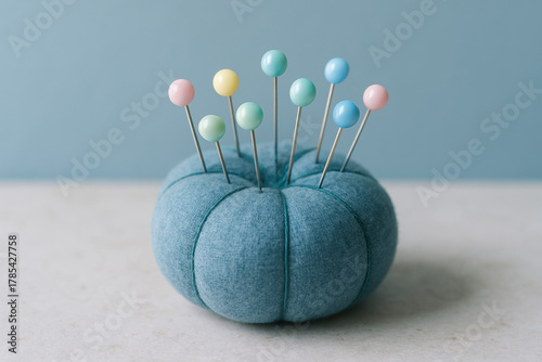 Soft blue pincushion with colorful round headed sewing pins arranged neatly on a light surface, minimal home craft concept