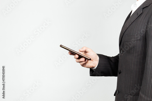 a businessman on suit at the right side of the screen holding a smart phone with his hand and a white background