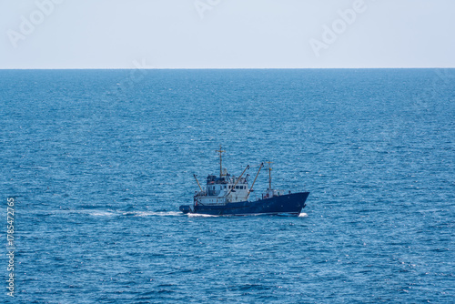Fishing boat in blue sea and clear sky with birds flying overhead.