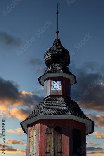 Bell tower with old mechanical clock with Roman numerals and only an hour hand against sunset sky. Church of St Lawrence, Pernio, Finland.