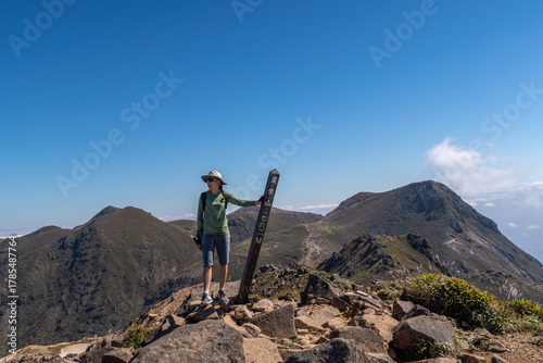 A female hiker standing on the summit of Mt. Tengugajo in Aso-Kuju National Park, Japan, looking thoughtfully to the side after a long mountain hike. Peaceful moment of reflection, nature appreciation