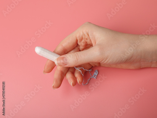 Female hand holding a white tampon on a pink background. Feminine hygiene product, menstruation and women’s health concept.