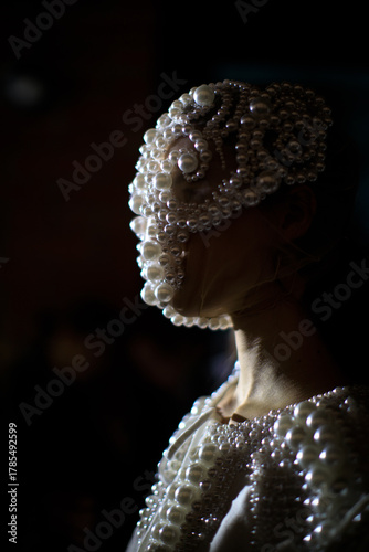 Close-up portrait of a model wearing an avant-garde pearl mask and dress, dramatic low light fashion concept