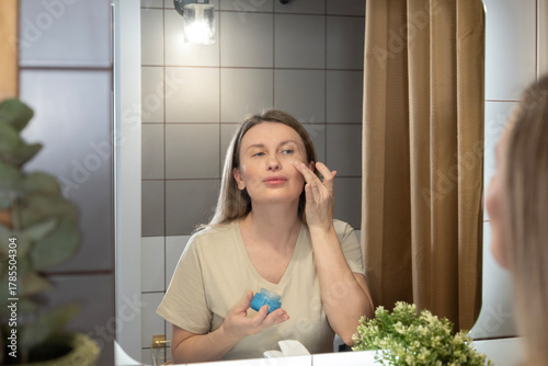 A daily beauty ritual. A woman applies moisturizer to her face in the bathroom, taking care of her skin and maintaining its youthfulness. Morning care, a healthy lifestyle, and self-improvement in det
