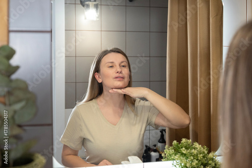 A daily beauty ritual. A woman applies moisturizer to her face in the bathroom, taking care of her skin and maintaining its youthfulness. Morning care, a healthy lifestyle, and self-improvement in det