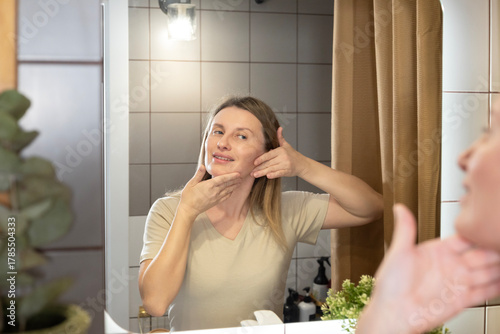 A daily beauty ritual. A woman applies moisturizer to her face in the bathroom, taking care of her skin and maintaining its youthfulness. Morning care, a healthy lifestyle, and self-improvement in det