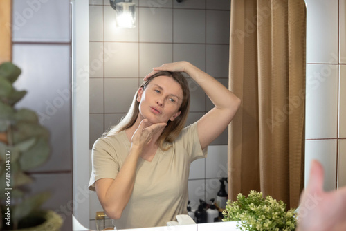 A daily beauty ritual. A woman applies moisturizer to her face in the bathroom, taking care of her skin and maintaining its youthfulness. Morning care, a healthy lifestyle, and self-improvement in det