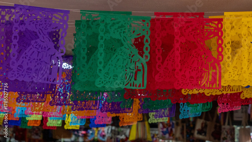 A colorful display of paper lanterns hang from the ceiling. The lanterns are in various colors. Mexican Day of the Dead tradition, offerings, food, colors, decorations, and papel picado, La Catrina.