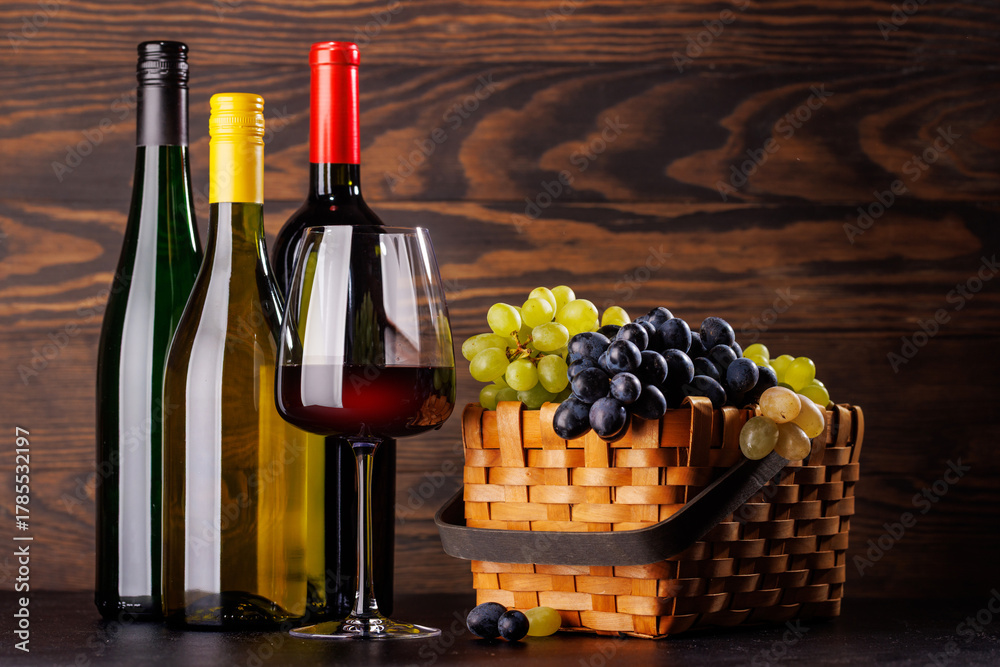 Naklejka premium Red and white wine bottles with a glass and basket of fresh grapes