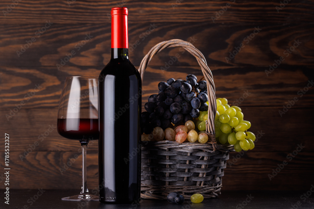 Naklejka premium Red wine bottle with a glass and basket of fresh grapes
