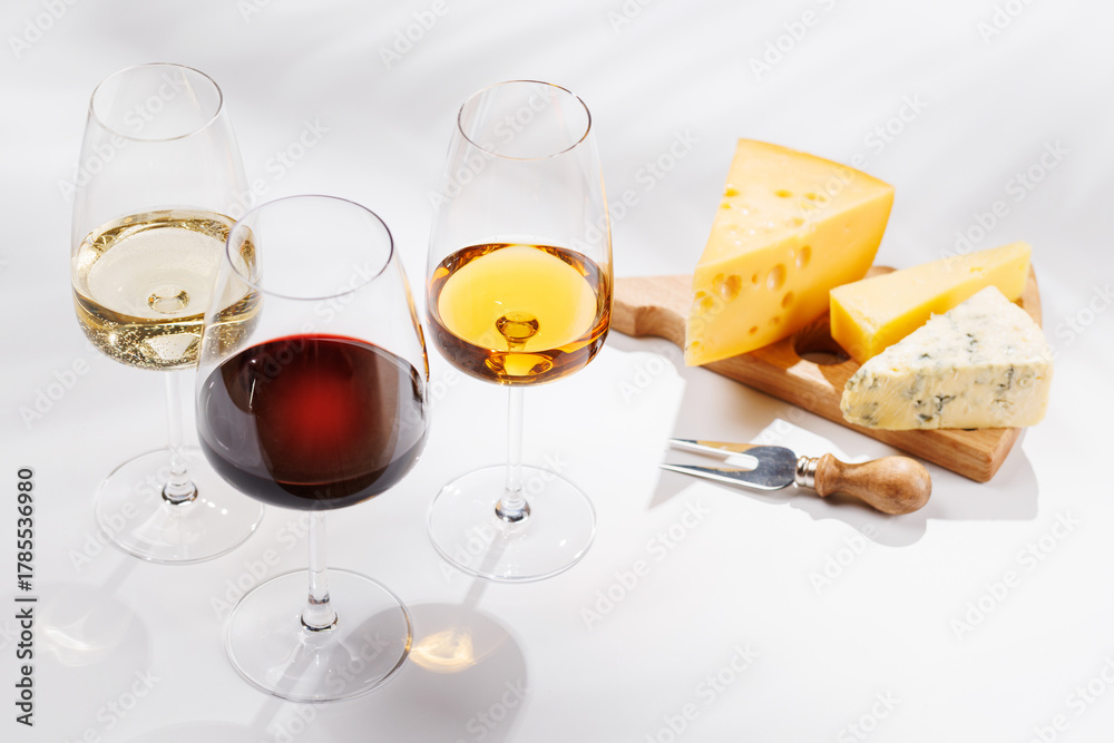 Fototapeta premium Assorted cheeses and wine glasses on white background
