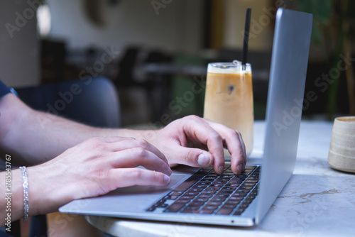 Male hands working with laptop and coffee cup on round table in outdoor cafe.