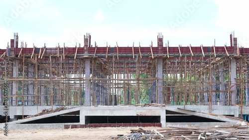 Construction site with concrete structure, wooden scaffolding, steel reinforcement, and unfinished building under blue sky, showing progress and industrial atmosphere, modern architecture development