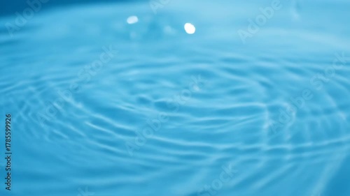 Slow Motion Water Drop Creating Concentric Ripples on a Blue Surface.