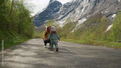 mall child joyfully runs toward her mom at the base of the majestic Trollstigen mountains in Norway. Scenic family moment surrounded by dramatic Nordic nature and rocky peaks.