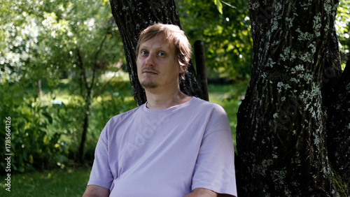 Relaxing man in a park on a bench in summer, enjoying the fresh air, vacation, or relaxing alone in the garden. A thoughtful, smiling, or calm man in nature, resting or waiting in a natural setting.