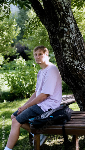 Relaxing man in a park on a bench in summer, enjoying the fresh air, vacation, or relaxing alone in the garden. A thoughtful, smiling, or calm man in nature, resting or waiting in a natural setting.