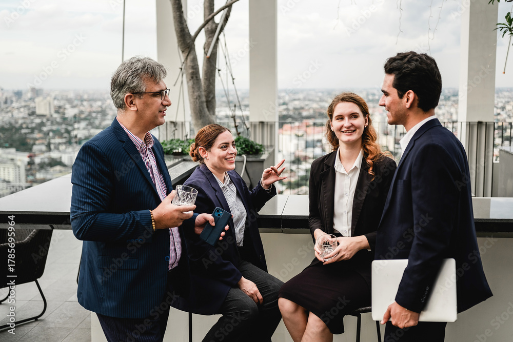 Obraz premium Four professionals network on a rooftop terrace, sharing drinks and conversation with a city skyline in the background.