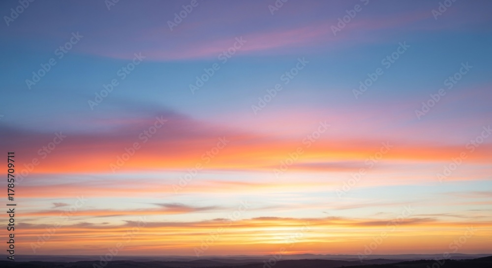 Obraz premium A vibrant sunset with a colorful sky and clouds, featuring a mix of warm and cool tones, with a mountain range in the background.