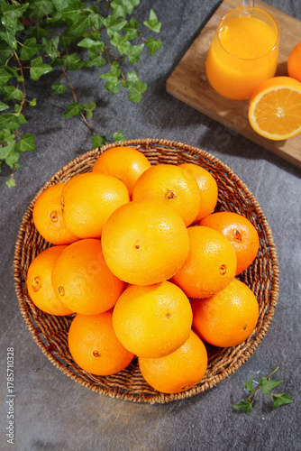 Fresh Navel Oranges in Wicker Basket with Orange Juice on Stone Surface