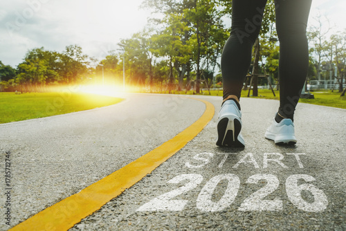 New Year 2026 concept. The beginning of success. The text 2026 is written on a paved road and a female runner is starting a new year. Concept of challenges or career paths and changes coming year.