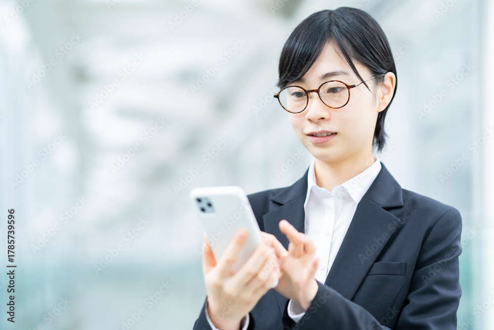 Obraz premium スマートフォンを操作するスーツ姿の若い女性