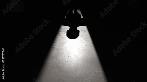 Dramatic low-angle shot of a man walking into a beam of light, casting a long shadow on the floor. Strong visual contrast and copy space enhance the mysterious tone